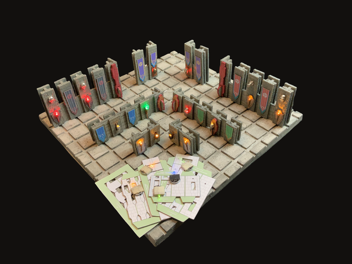 A miniature tabletop gaming terrain piece showing a stone-tiled room with many gray doorways and panels, some glowing with red, blue, green, and orange lights, plus scattered cards or papers placed in front, all photographed on a black background.